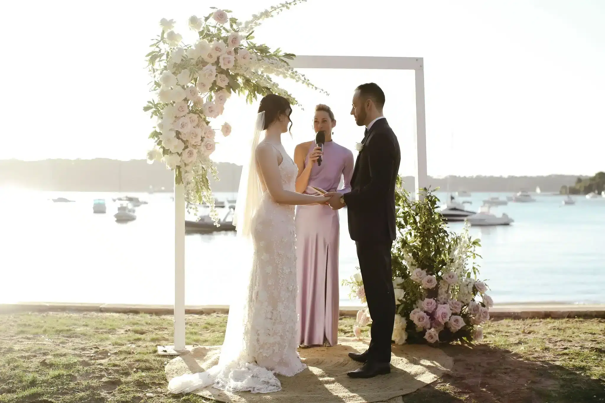 NatashaJosh_PrintFiles-357 A couple holding hands as they get married under the arbour by Jacqua Celebrant at Watson's Bay, Sydney